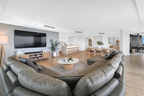 Ein modernes Wohnzimmer mit einem großen Flachbildfernseher, Ledersofas, einem Couchtisch und einem Essbereich mit Holztischen und -stühlen.
