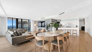 Una sala moderna con sofá, mesa de comedor y sillas, zona de cocina y ventanas grandes con vistas.