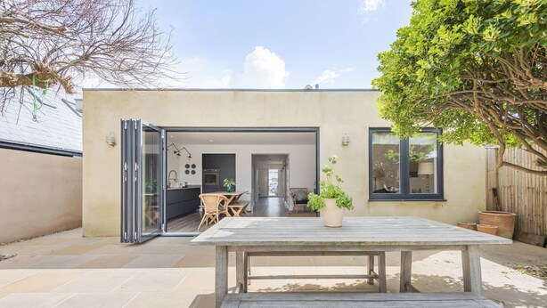 Una casa moderna con un patio, una mesa de comedor y una cocina visible a través de la puerta abierta.