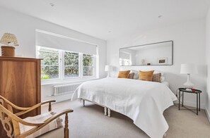 Ein Schlafzimmer mit großem Fenster, einem Bett, einem Holzstuhl, einem Nachttisch und einem Spiegel.