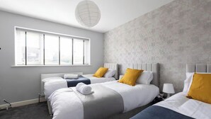 Quarto de hotel com duas camas, um radiador, uma janela com persianas e uma parede com textura.
