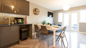 Uma cozinha moderna com armários escuros, painel de azulejos em padrão herringbone e uma área de jantar com mesa e cadeiras brancas.