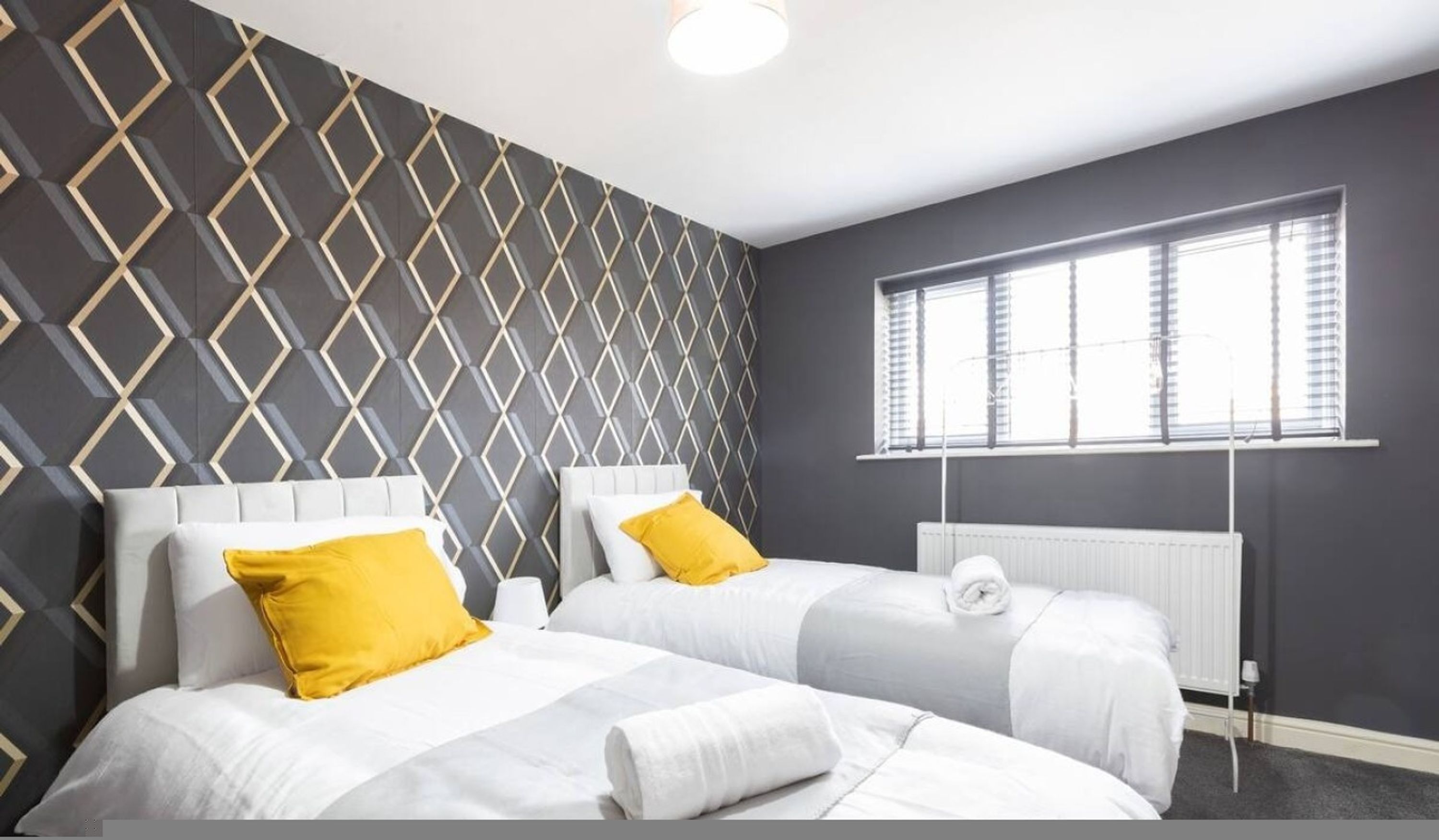 A hotel room with two beds, a radiator, and a window with blinds.