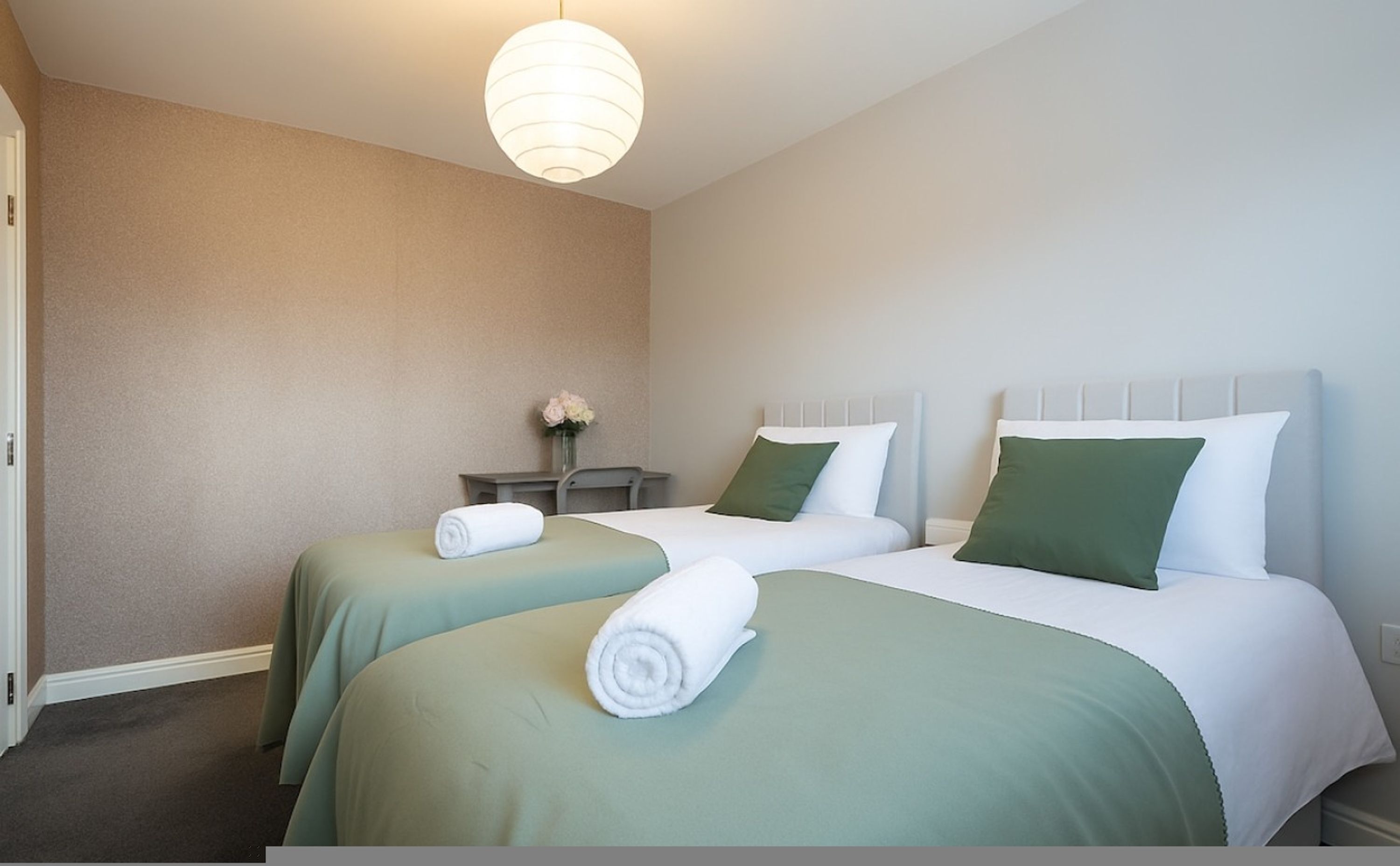 Een hotelkamer met twee bedden, een nachtkastje, een vaas met bloemen en een hanglamp.