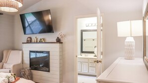 Ein Schlafzimmer mit Fernseher, Kamin, Bett und einem Badezimmer mit Spiegel und Waschbecken.