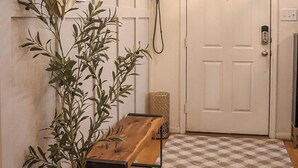 Ein Flur mit Holzboden, einem Schachbrettteppich, einer Topfpflanze, einer Pendelleuchte und einer Tür mit Zahlenschloss.
