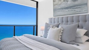 A bedroom with a large window overlooking the ocean, a tufted headboard, and a painting above the bed. - Ocean Skyhome at Oracle Level 40 (Gold Coast City)