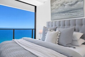 Ein Schlafzimmer mit großem Fenster und Meerblick, einem rautenförmig geprägten Kopfteil und einem Gemälde über dem Bett.
