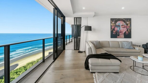 A modern living room with a large window overlooking a beach, a sofa, and a painting on the wall. - Ocean Skyhome at Oracle Level 40 (Gold Coast City)