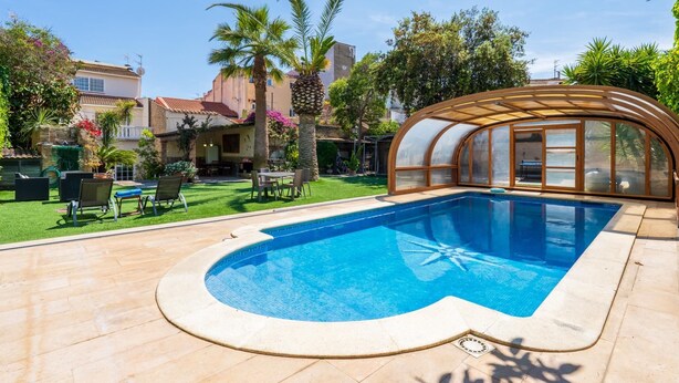 Ein Pool mit einer eingelassenen Sitzecke, umgeben von Palmen und einer überdachten Terrasse.