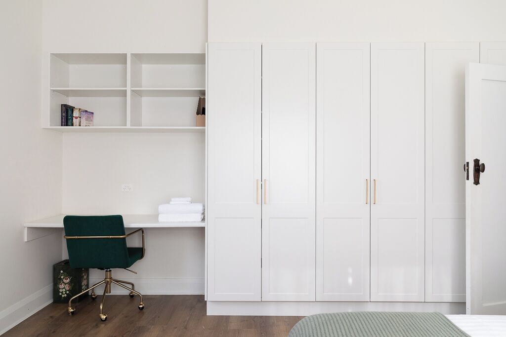 A bedroom with a bed, a desk with a chair, a wardrobe, and a shelf with books.