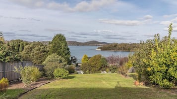 A backyard with a lawn, trees, and a view of a lake.