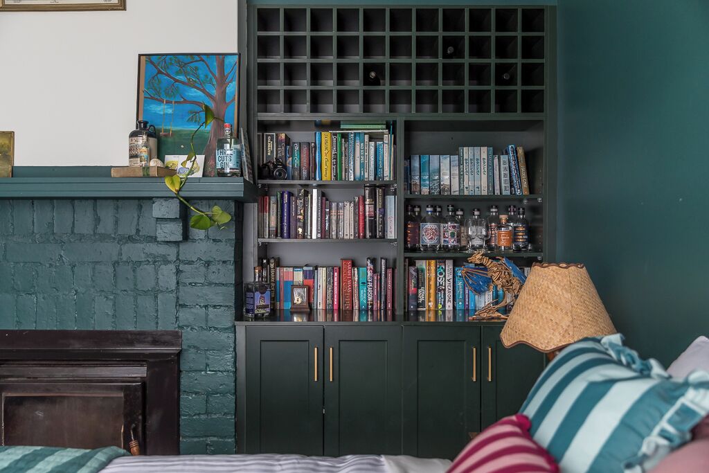A room with a dark green bookshelf filled with books and decorative items, a wooden headboard, and a striped pillow on the bed.