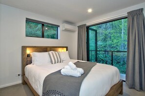 Un dormitorio con una cama grande, cabecera, ventana con cortinas y equipo de aire acondicionado.
