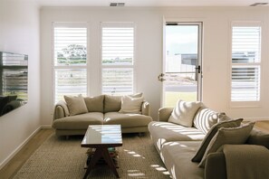 Ein Wohnzimmer mit einem beigen Sofa, einem Couchtisch und einer zur Außenwelt führenden Tür.