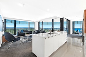 Eine moderne Wohnung mit einer großen Kücheninsel, einem Wohnbereich mit Sofa und Sesseln sowie großen Fenstern mit Blick auf die Stadt.