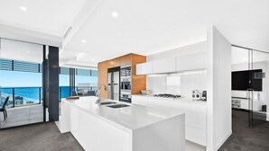 Une cuisine moderne dotée d’un grand îlot central, d’appareils électroménagers intégrés et offrant une vue sur l’océan.