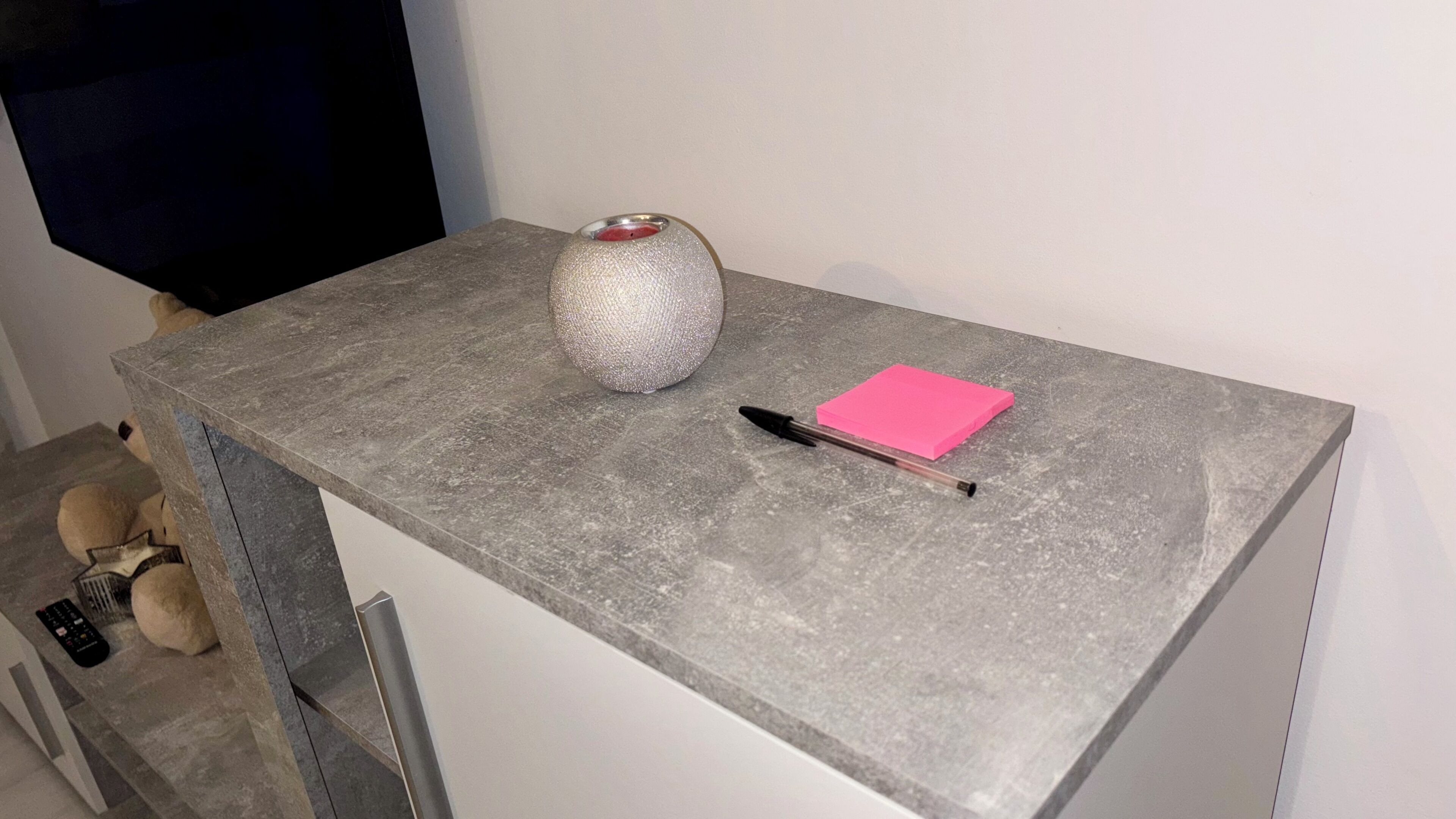 A grey stone table with a silver textured vase, a pink sticky note, and a black pen.