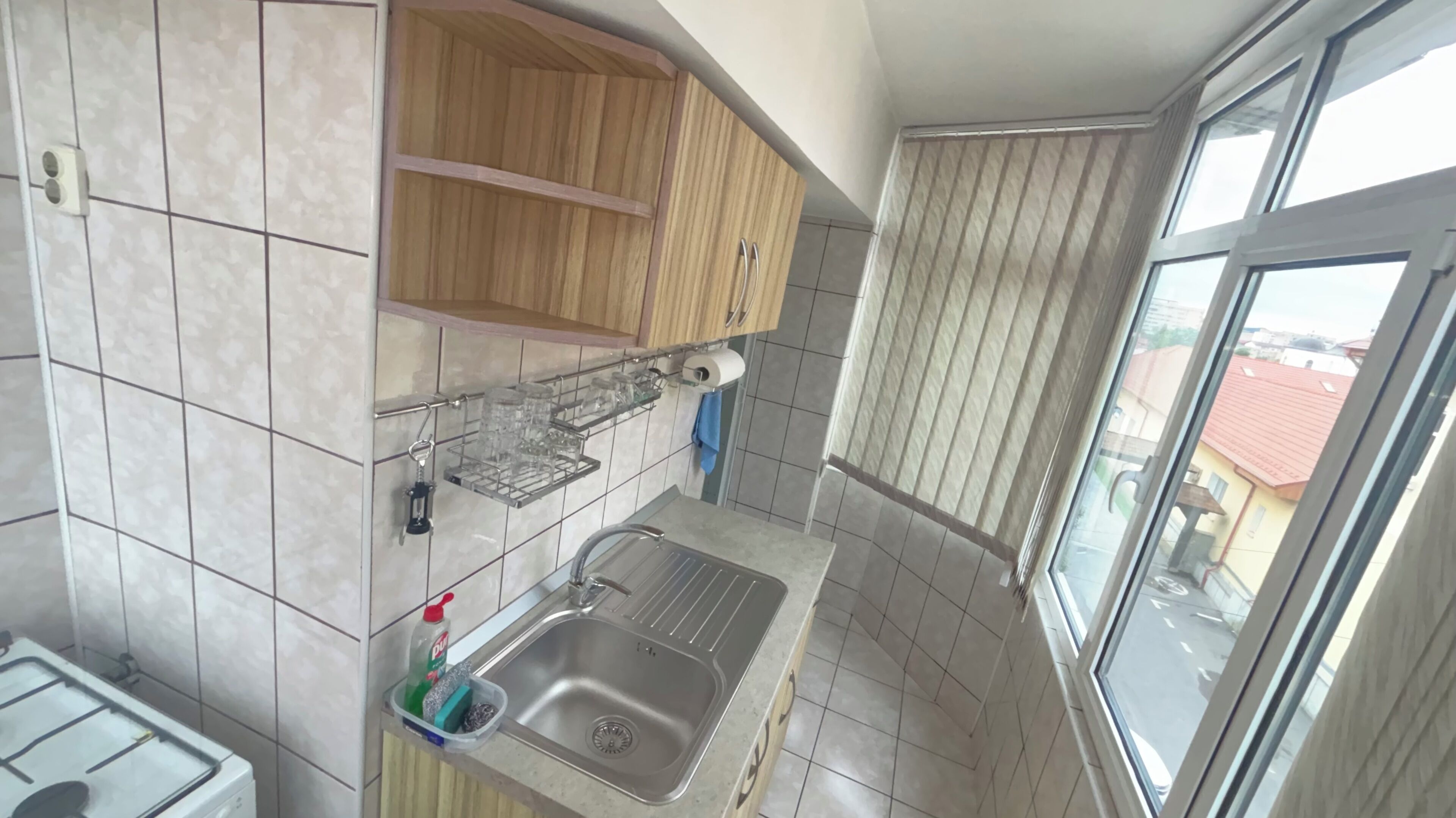 A kitchen with a sink, wooden cabinets, a window, and a view of buildings outside.
