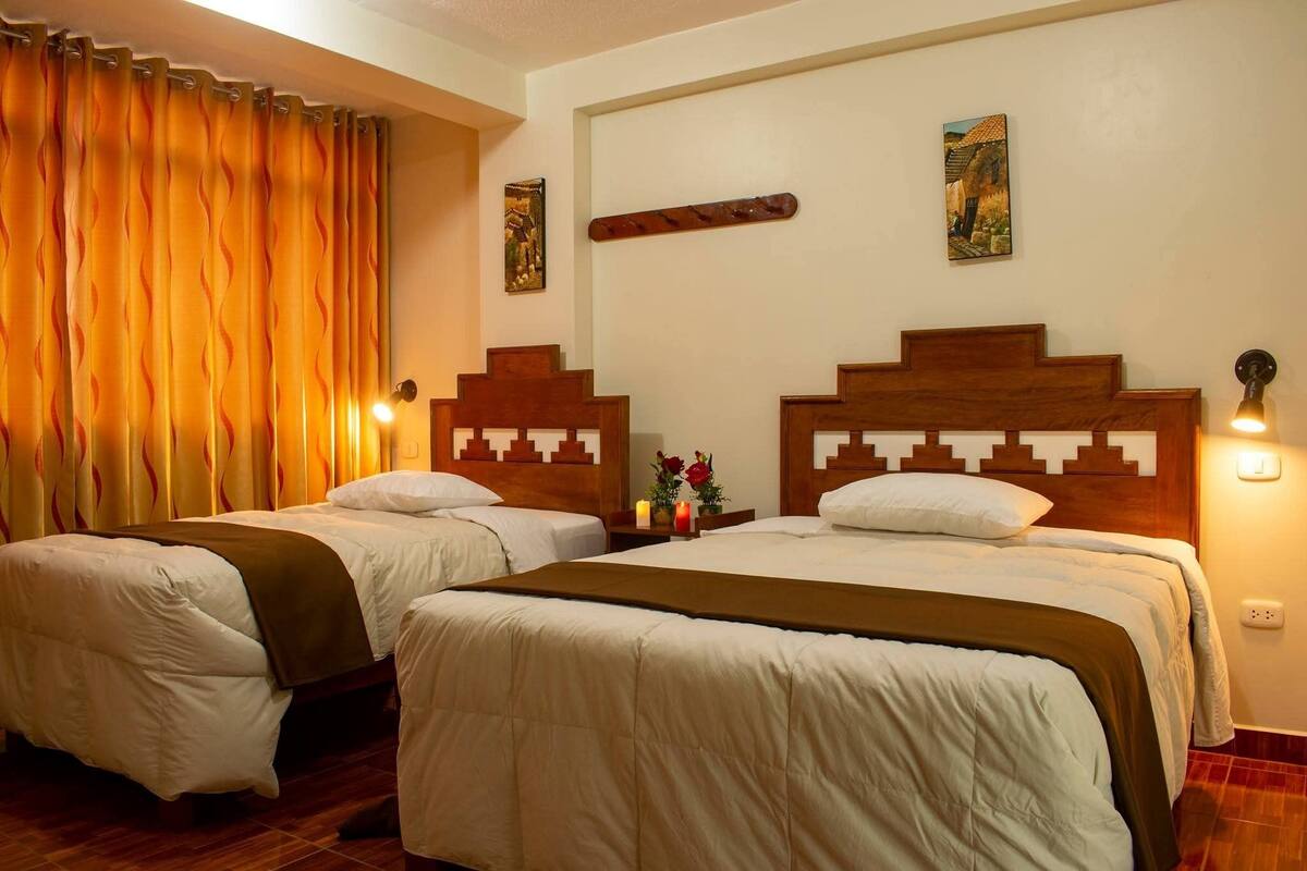 Habitación de hotel con dos camas, cabeceros de madera, una mesita de noche con un florero y una obra de arte en la pared.