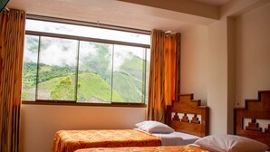 Quarto com duas camas, uma janela grande com cortinas e vista para colinas verdes.