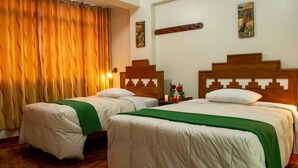 Habitación de hotel con dos camas, cabeceros de madera, ropa de cama blanca, un plaid verde y una cortina.