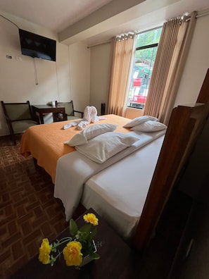 A hotel room with a bed, a desk, a chair, a TV, and a window with curtains.