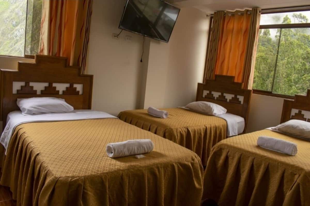 Una habitación con dos camas, cada una con cabecera, un televisor de pantalla plana montado en la pared y una ventana con cortinas.