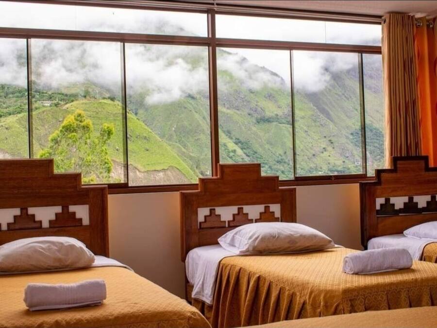 A hotel room with three beds, a large window with a mountain view, and a wooden headboard design.