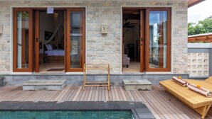 A modern house with a pool, wooden deck, and large glass doors leading to a bedroom and bathroom. - Janu Villa (Ubud)