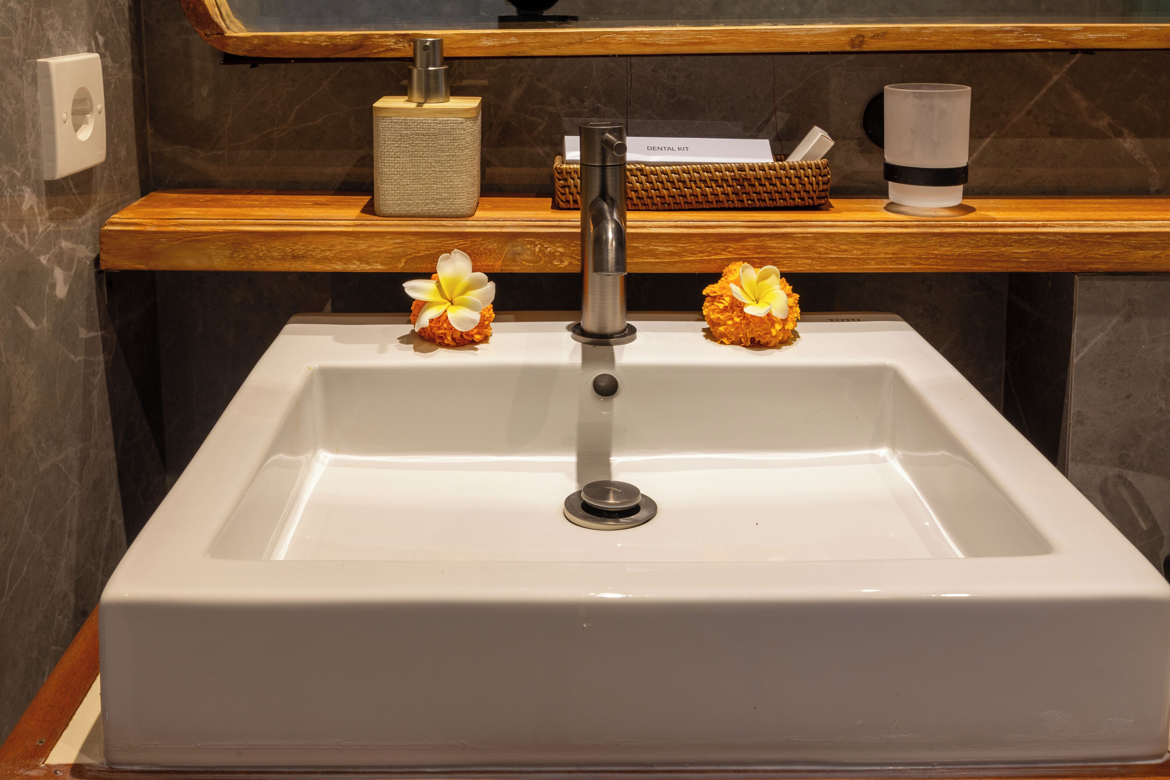 Ein Badezimmer mit einem weißen Waschbecken, einem Holzboden mit einem Korb, einem Taschentuchspender und einem Kerzenhalter.