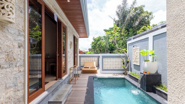 A pool area with a wooden deck, a lounge chair, and a small waterfall feature. - Janu Villa (Ubud)
