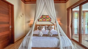 A bedroom with a canopy bed, a stained glass window, and a view through a glass door. - Janu Villa (Ubud)