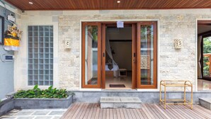 A building entrance with a wooden door, a small step leading up, and a metal rack outside. - Janu Villa (Ubud)