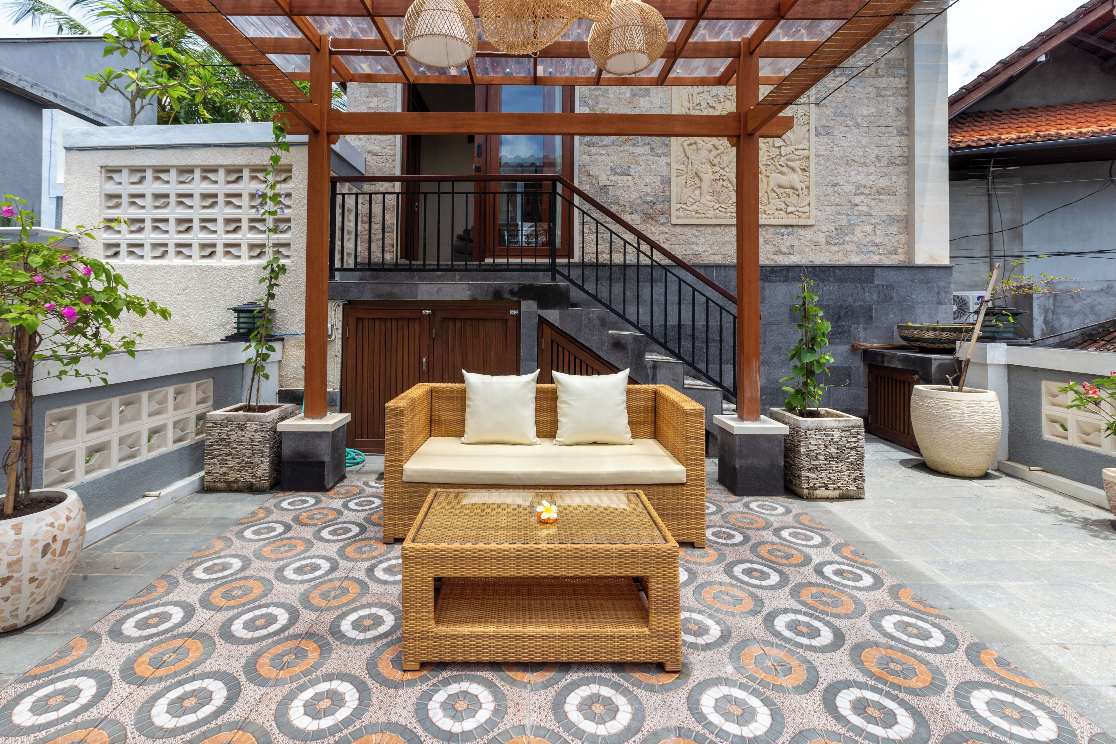 Un espacio al aire libre cubierto con sofá, mesa, escalera y plantas decorativas.