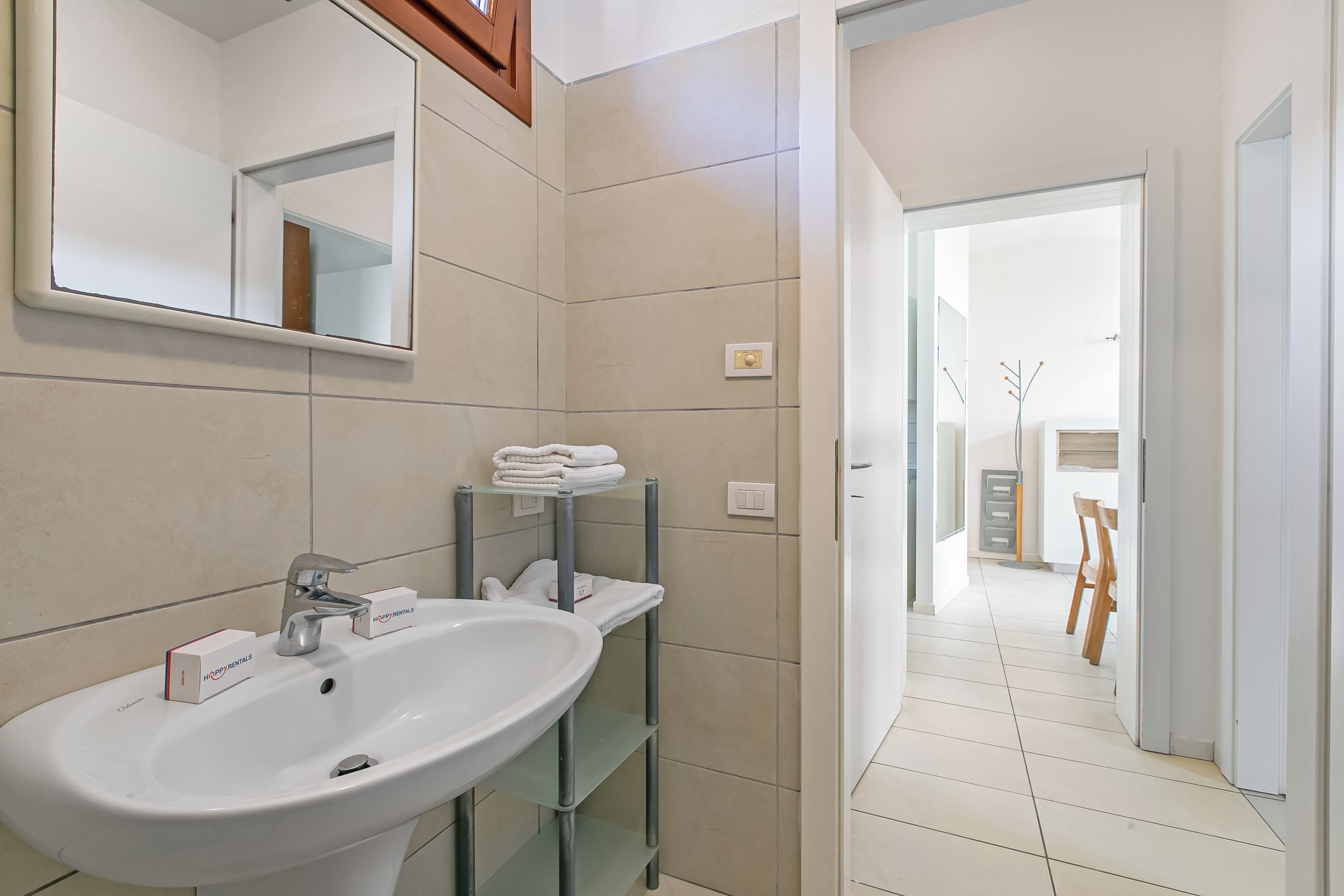 Un baño con lavamanos, espejo y repisas con toallas dobladas.