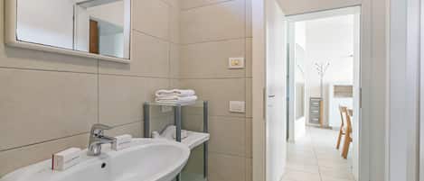 Un baño con lavamanos, espejo y repisas con toallas dobladas.