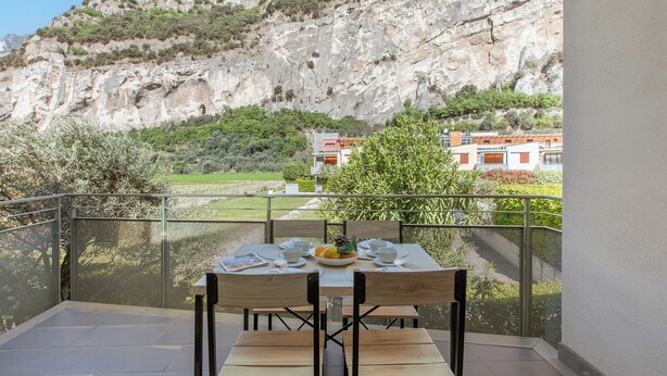 A balcony with a table set for two, overlooking a mountainous landscape. - Garda Therme Apartment With Balcony & Mountain Views (Arco)