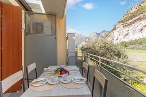 A balcony with a table set for dining, overlooking a mountainous landscape. - Garda Therme Apartment With Balcony & Mountain Views (Arco)