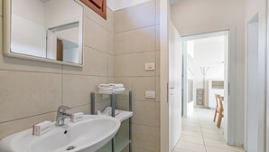 A bathroom with a sink, mirror, and shelves with folded towels. - Garda Therme Apartment With Balcony & Mountain Views (Arco)