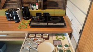 Una cocina equipada con tostadora, cafetera, estufa y un cajón con varios platos y tazas.