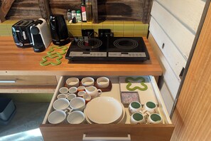 A kitchen with a toaster, coffee maker, stove, and a drawer with various dishes and cups.