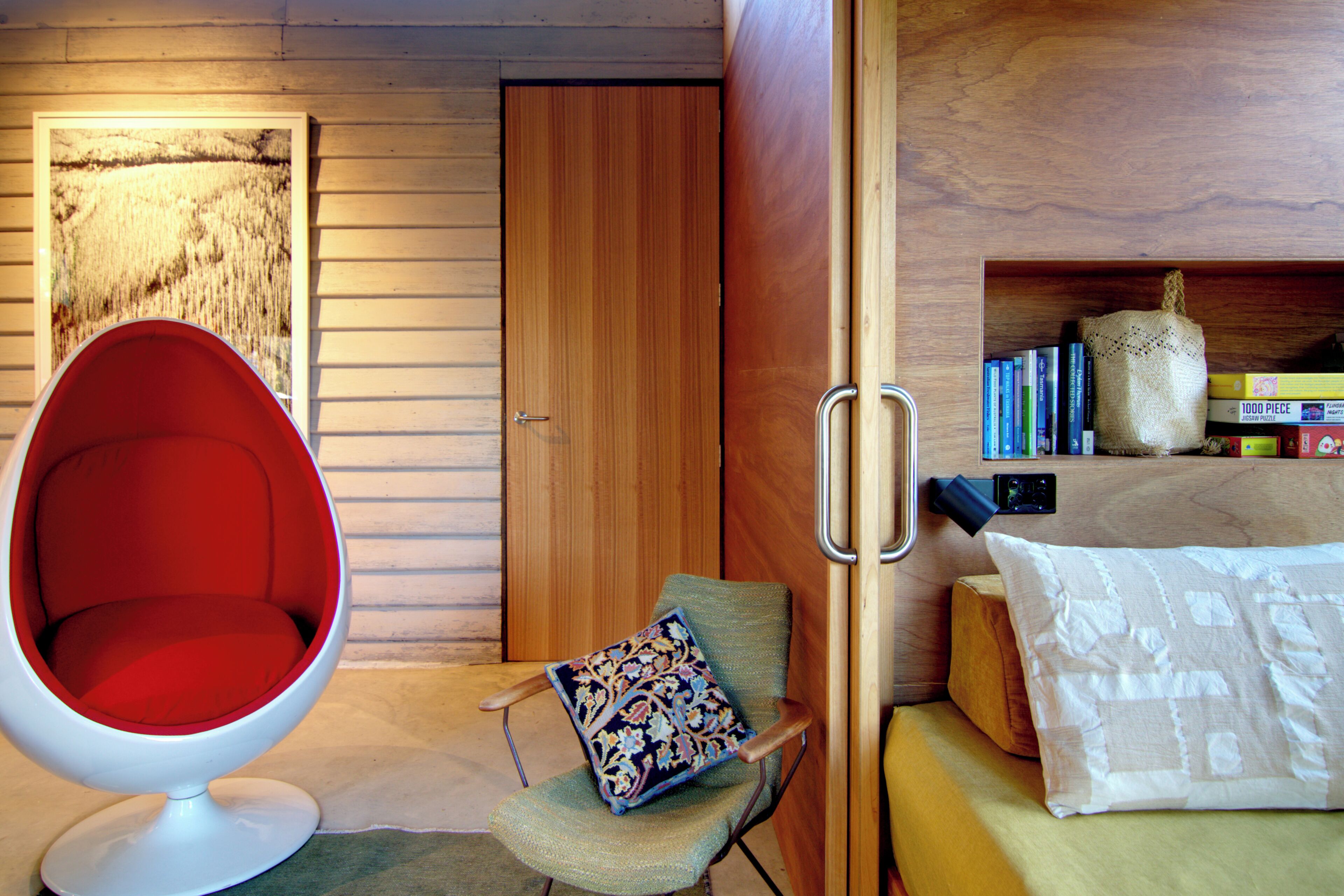 A room with a red chair, a wooden door, a bookshelf with books, and a jigsaw puzzle box.