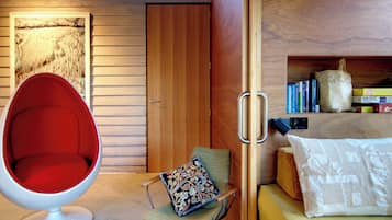 A room with a red chair, a wooden door, a bookshelf with books, and a jigsaw puzzle box.