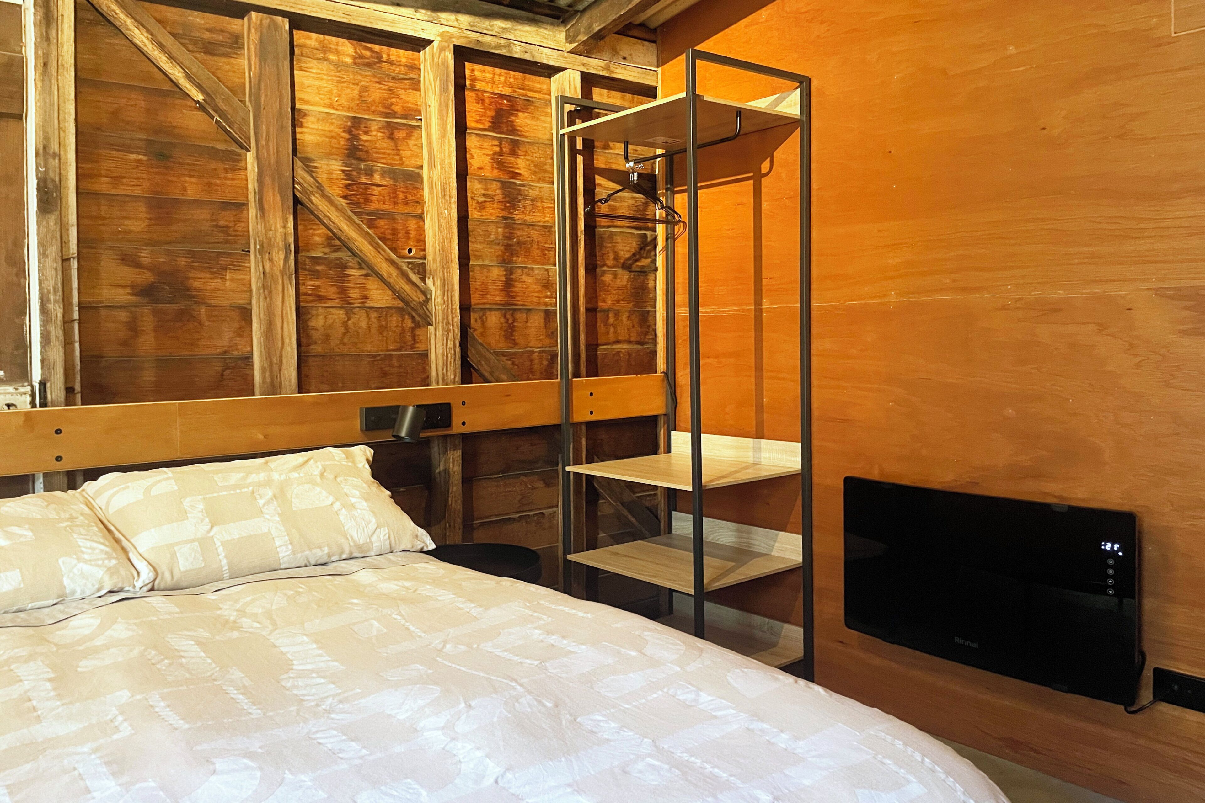 Une chambre avec un lit, un mur en bois, une étagère en métal et un téléviseur.