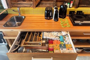 A kitchen with a wooden countertop, a sink, a toaster, a kettle, and a drawer with utensils and coffee pods.