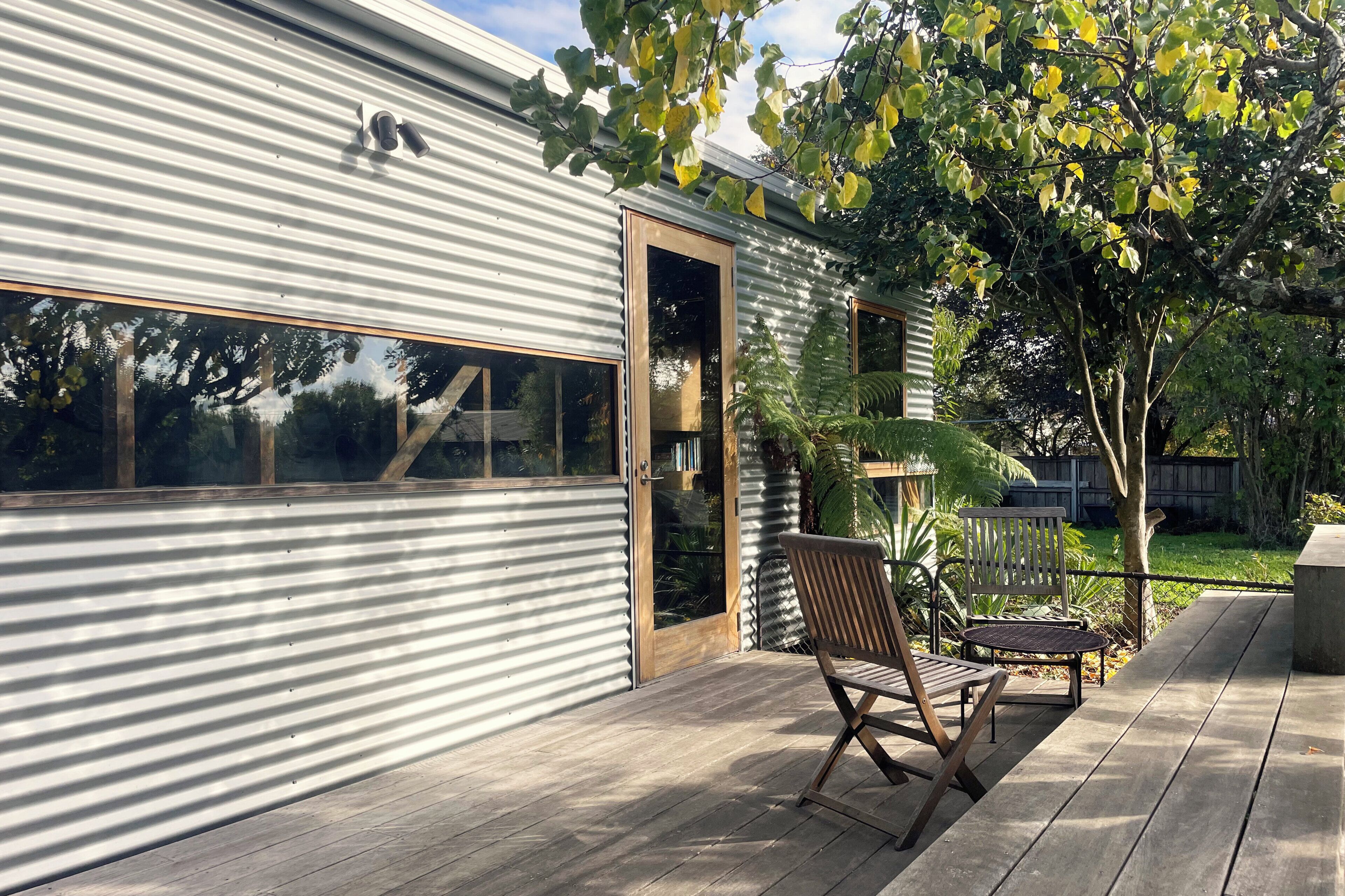 A modern building with a corrugated metal exterior, a wooden deck, and a seating area with a chair and table.