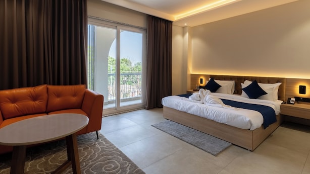A hotel room with a bed, a sofa, a table, and a view of the outdoors. - The Archway Hotel (Haldwani)