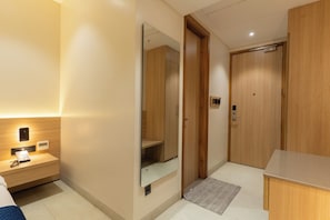 A hotel room with a wooden wardrobe, a bedside table with a phone, a mirror, and a small rug. - The Archway Hotel (Haldwani)