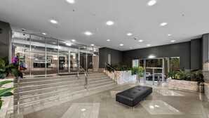 A modern lobby with a marble floor, a black bench, glass doors, and a staircase leading to an upper level. - Exclusive Stays - Southgate (Southbank)